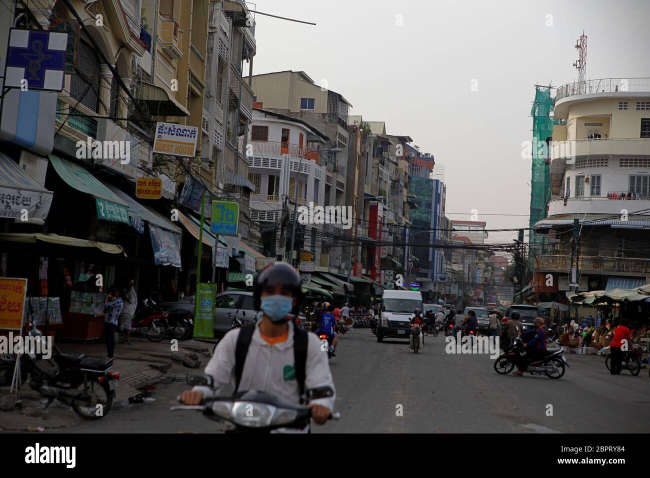 Un uomo che indossa la maschera facciale mentre sta guidando la motocicletta attraverso una zona di affari a Phnom Penh, Cambogia. Foto Stock