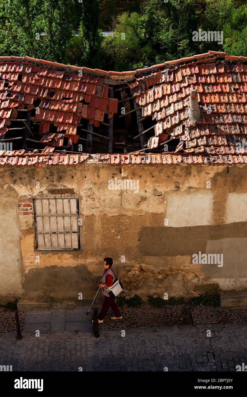 Donna che cammina indisturbata dall'edificio sbriciolato alla sua destra nella città vecchia di Cuenca, Spagna. Foto Stock