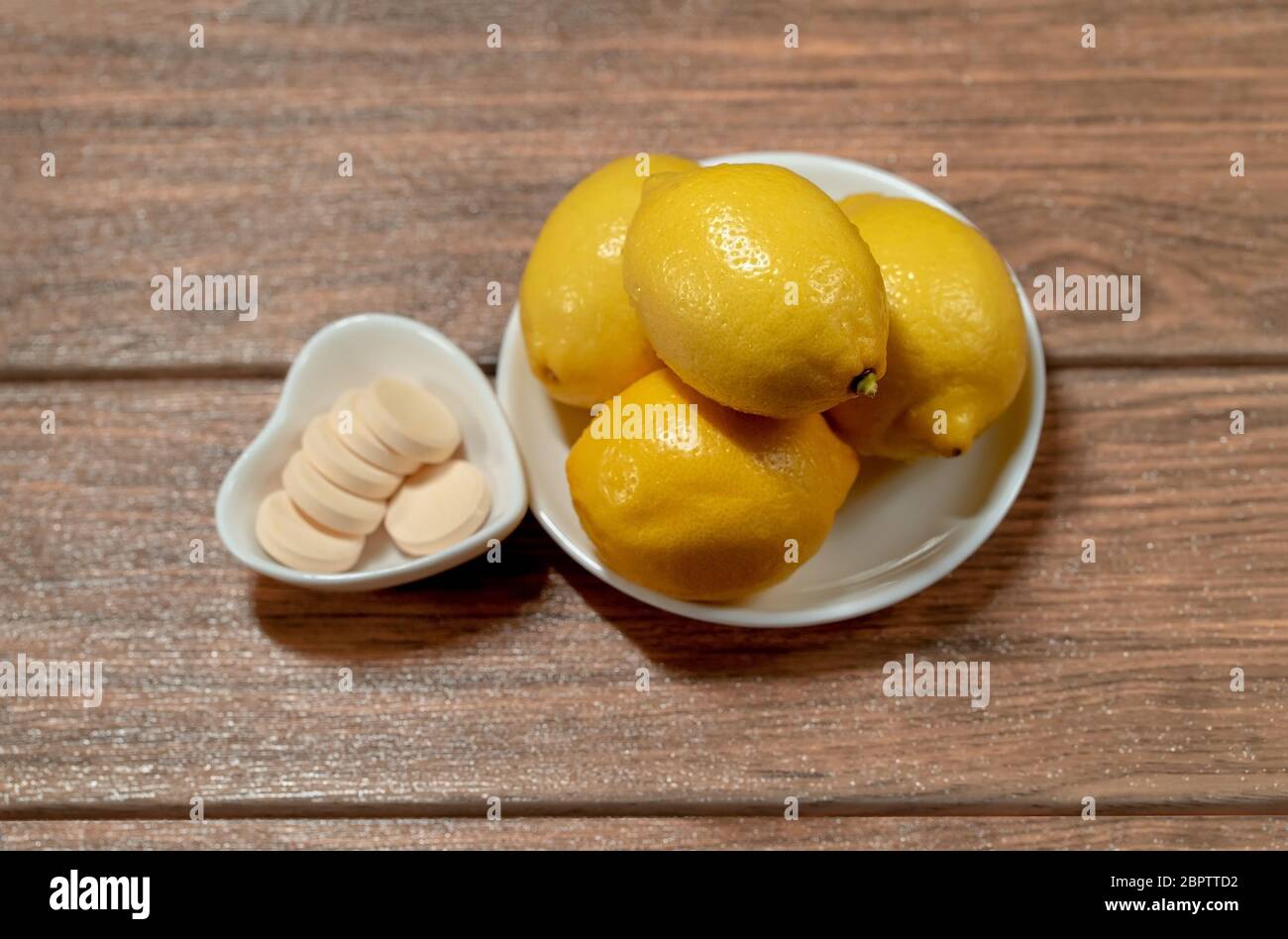 quattro limoni con compresse di vitamina c arancio in diversi piatti su un tavolo di legno vista dall'alto Foto Stock