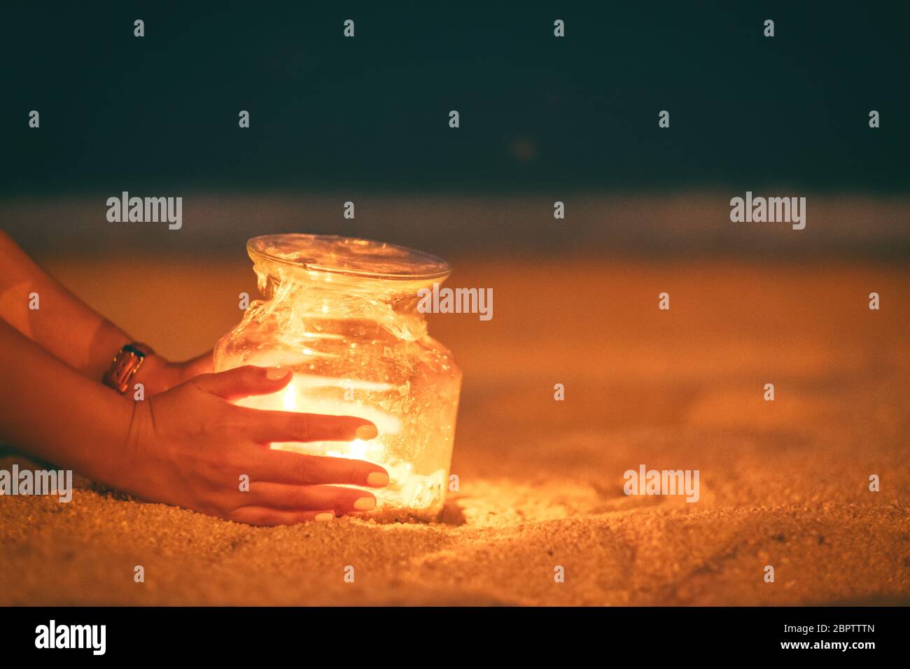 Immagine closeup di una donna che tiene e mette una bottiglia di vetro porta candele sulla spiaggia di notte Foto Stock