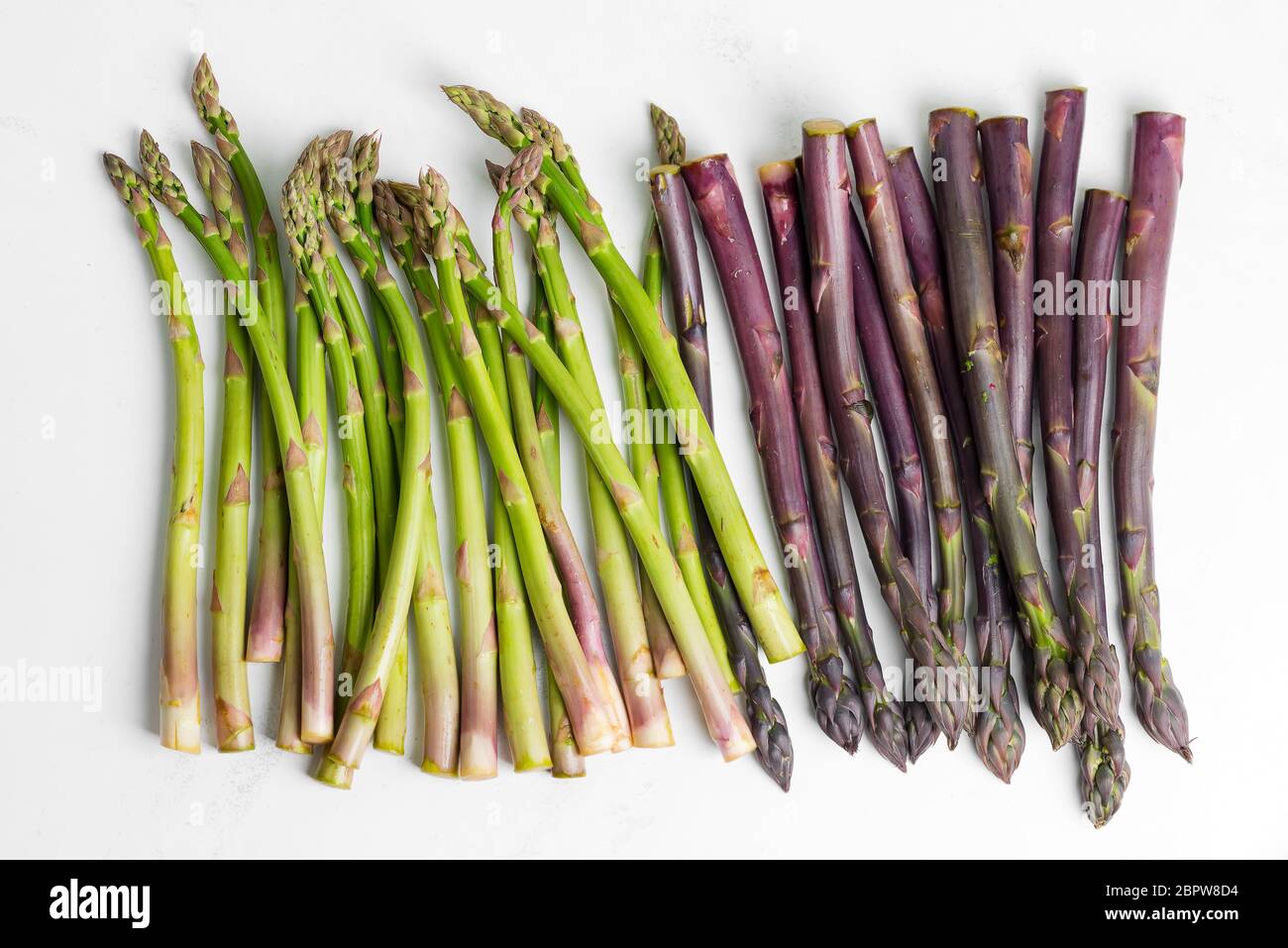Vista dall'alto sopra le lance di asparagi verdi e viola, preparate al momento, pronte per cucinare cibi vegetariani sani su una macina di pietra grigio chiaro Foto Stock