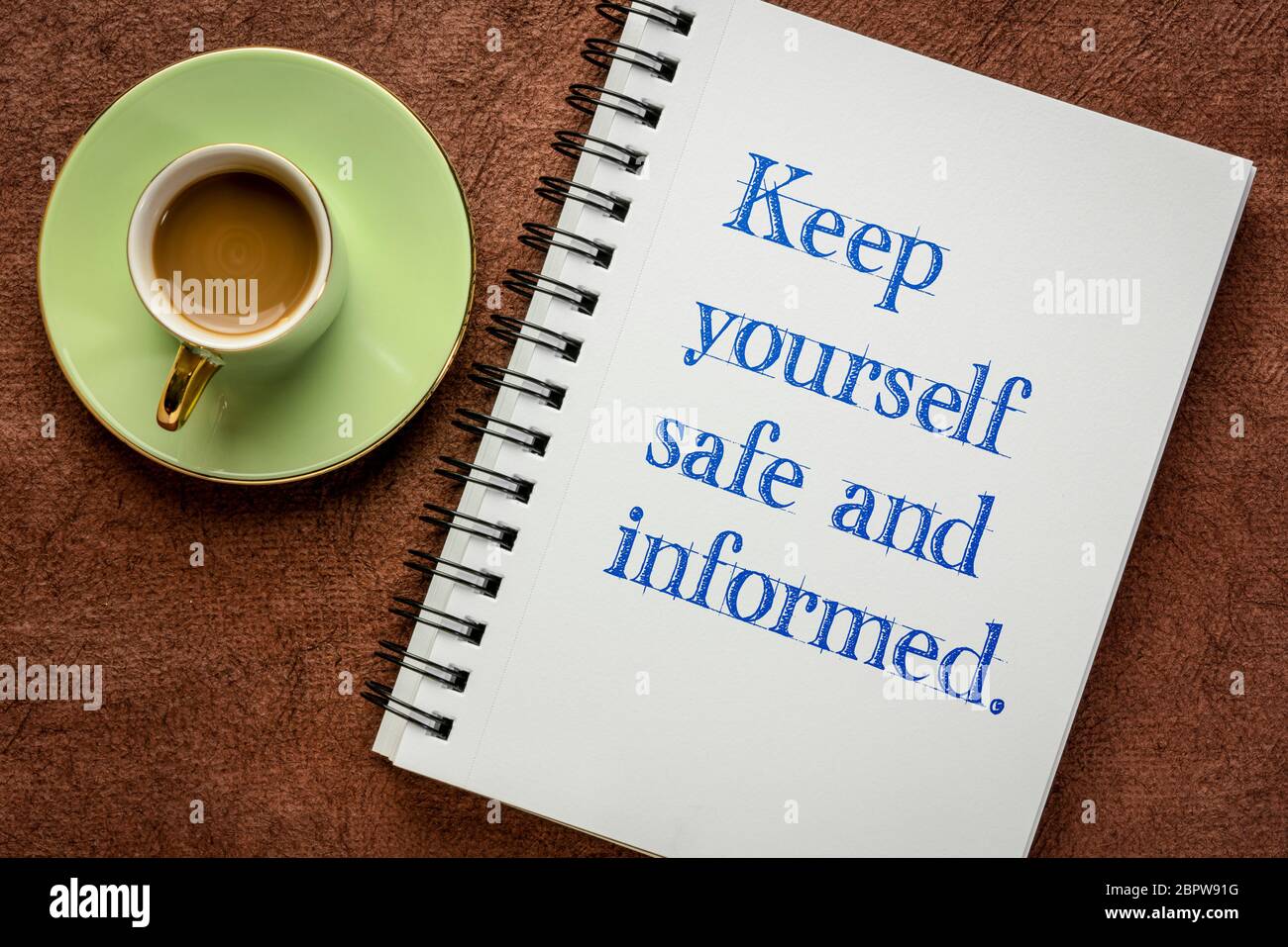 tieniti sicuro e informato: scrittura motivazionale in un notebook a spirale con una tazza di caffè, promemoria per la crisi pandemica del coronavirus Foto Stock
