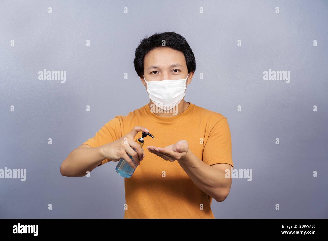 Uomo asiatico che indossa maschera chirurgica viso che presenta e utilizzando gel di alcol o disinfettante per le mani su sfondo blu, covid19 focolaio e pandemia, salute Foto Stock Uomo asiatico che indossa maschera chirurgica viso che presenta e utilizzando gel di alcol o disinfettante per le mani su sfondo blu, covid19 focolaio e pandemia, salute Foto Stock