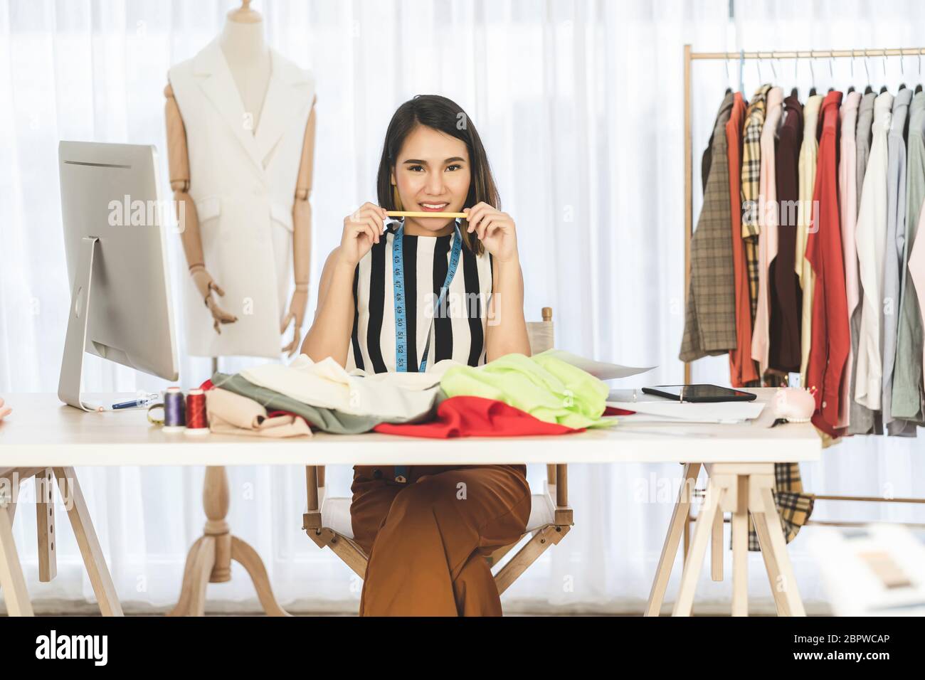 Ritratto di giovane donna asiatica designer che lavora e scegliendo abiti multicolore sul posto di lavoro, startup di piccole imprese, imprenditore proprietario di affari, moder Foto Stock