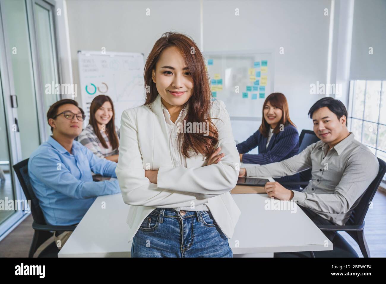 Ritratto di Asian Business Woman con armi incrociate e in piedi sul gruppo di collega partner quando brainstorming riunione sul posto di lavoro moderno, hu Foto Stock Ritratto di Asian Business Woman con armi incrociate e in piedi sul gruppo di collega partner quando brainstorming riunione sul posto di lavoro moderno, hu Foto Stock