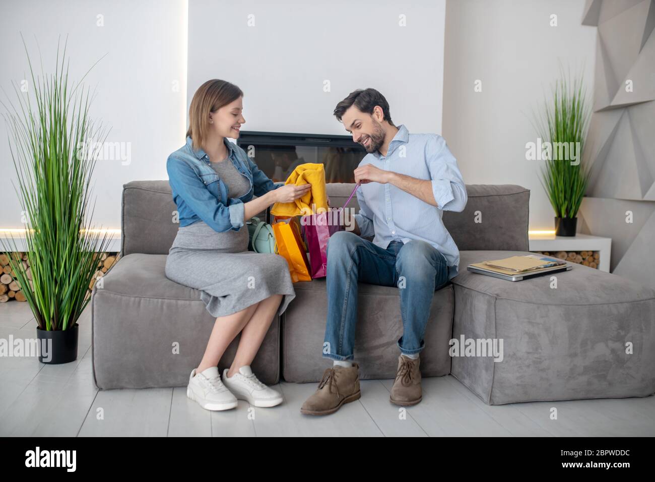 Giovane donna incinta che tiene una gonna gialla e ne discute con suo marito Foto Stock