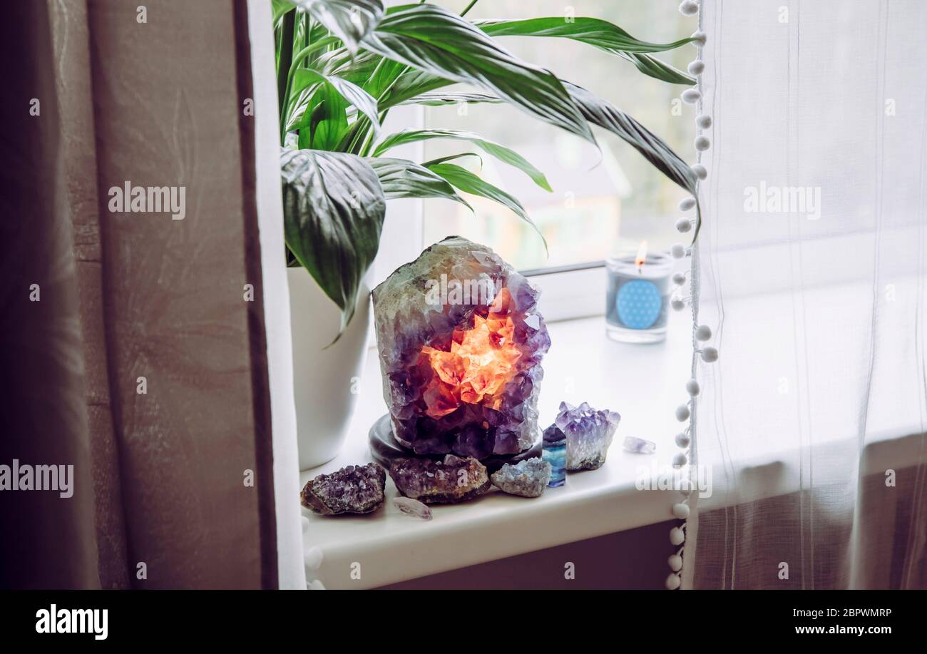 Utilizzando dettagli in cristallo di pietra semi-preziosi in concetto domestico. Lampada geode ametista bruciante, atmosfera spirituale calmante casa. Impianto pneumatico Spathiphyllum. Foto Stock