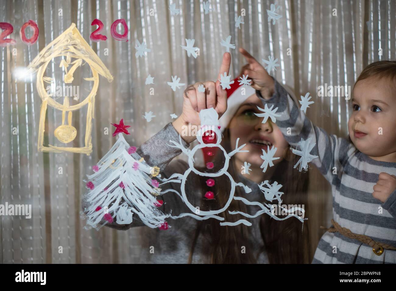 Mamma e figlia disegnano un pupazzo di neve, un albero di Natale e un  orologio con le pitture su una finestra pane. Disegno con acrilici su vetro  Foto stock - Alamy