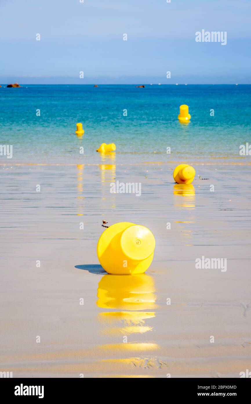 Cinque grandi boe gialle gialle gialle gialle sulla sabbia bagnata e galleggianti sul mare, delimitano un canale di lancio per piccole imbarcazioni sulla spiaggia in una giornata di sole. Foto Stock