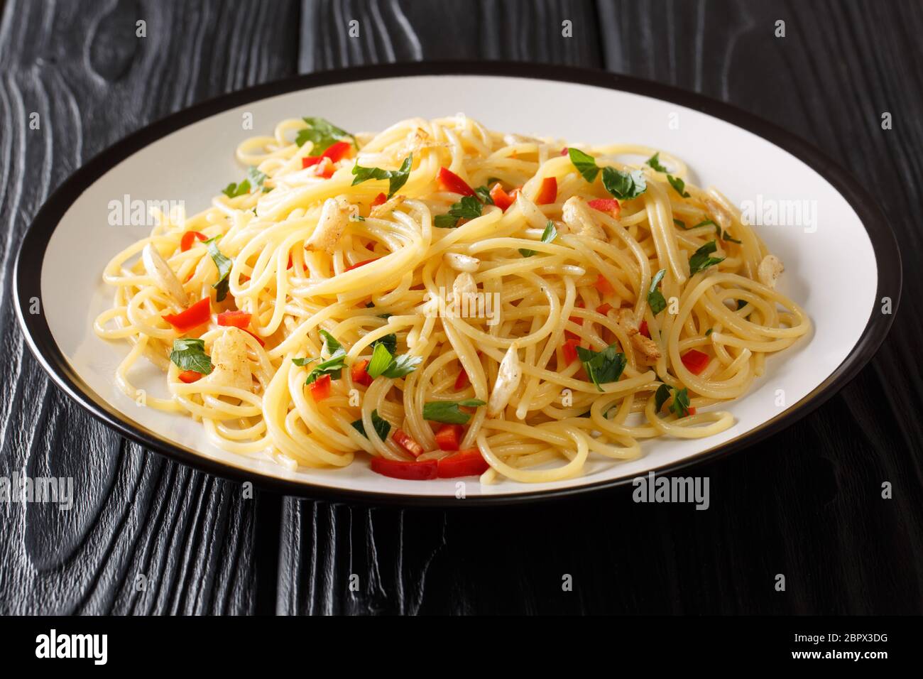Ricetta per la classica pasta di aglio e olio con aglio fritto, prezzemolo e pepe caldo primo piano in un piatto sul tavolo. Orizzontale Foto Stock
