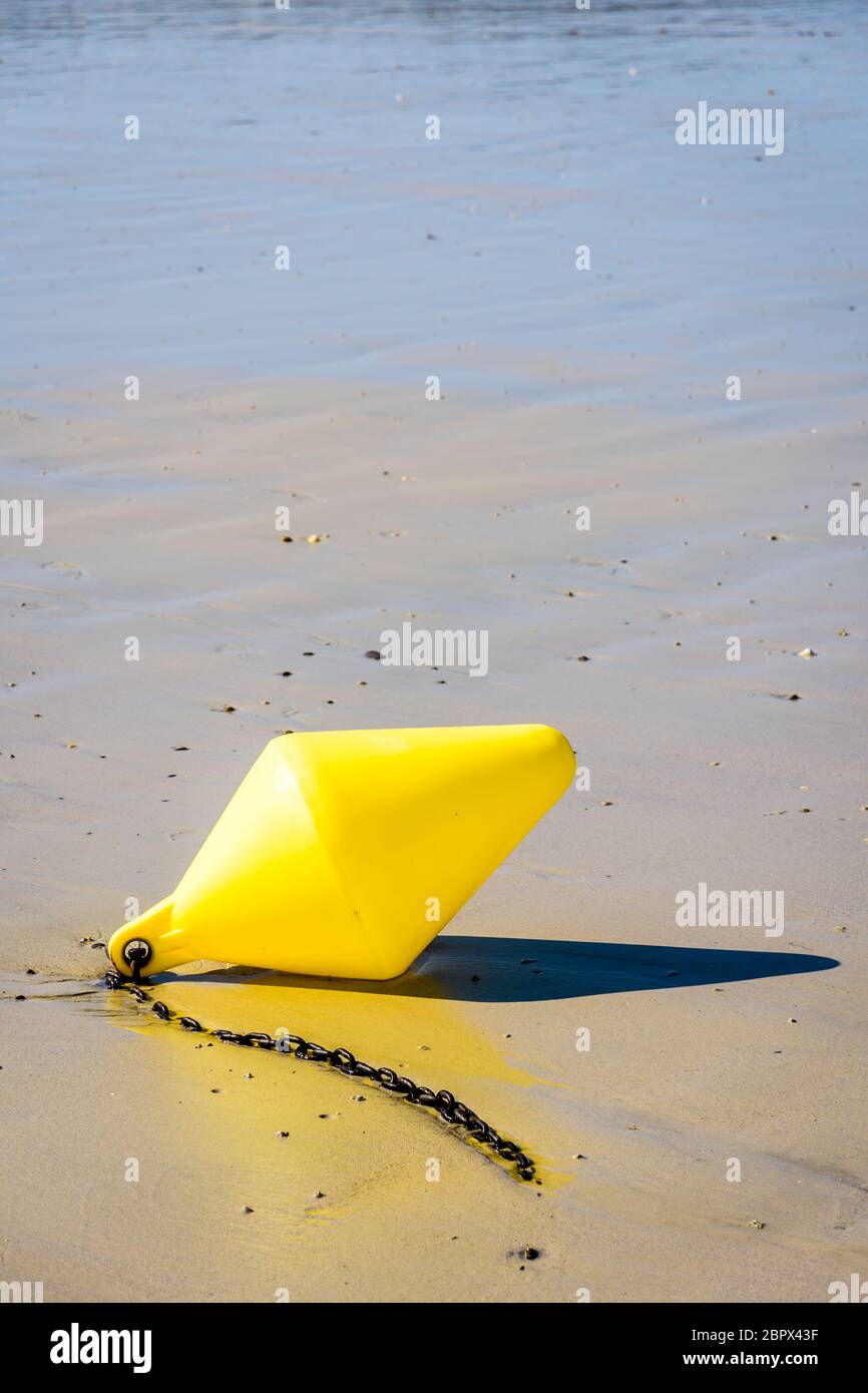 Una grande boa gialla e la sua catena di ancoraggio, utilizzata come marcatore di canale di lancio, giacente sulla sabbia bagnata a bassa marea sulla spiaggia al sole. Foto Stock