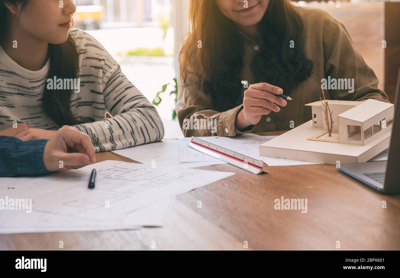 Gruppo di un architetto holding e discutere di un modello di architettura con disegno del negozio di carta sul tavolo in ufficio Foto Stock