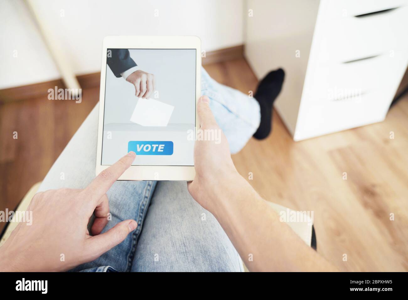 Uomo che voterà online a casa utilizzando il tablet digitale. Foto Stock