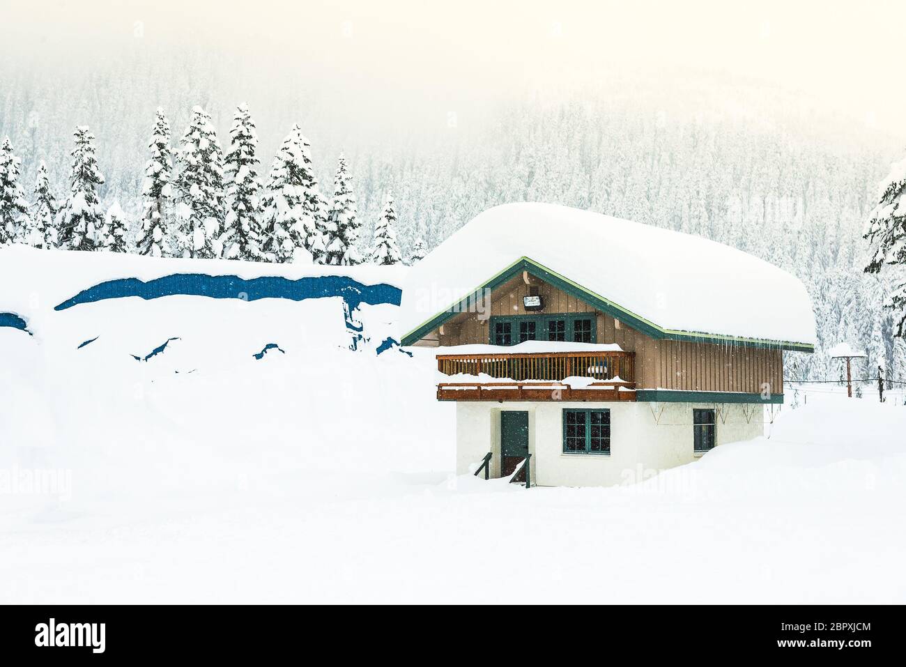 una casa coperta di neve fitta sul tetto con neve sfondo foresta quando il tramonto. Foto Stock