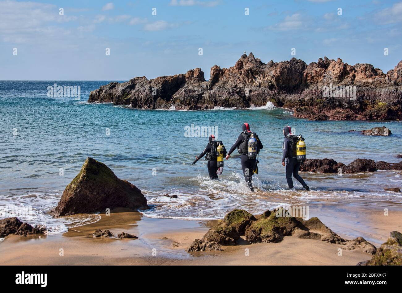 Tre subacquei entrano in mare nel piccolo porto di Lanzarote, Isole Canarie, Spagna Foto Stock