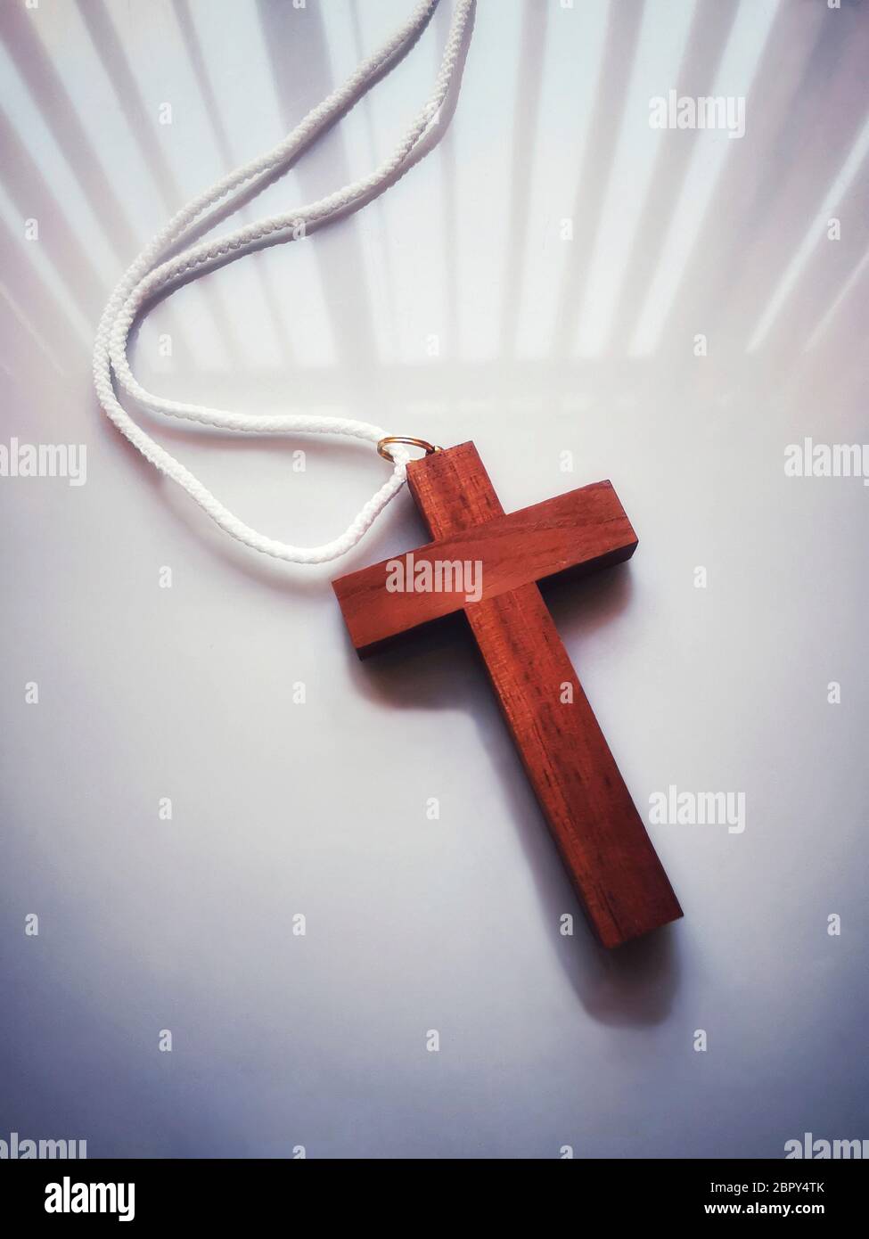 Colpo verticale ad angolo alto della croce di legno con una corda bianca su una superficie bianca Foto Stock