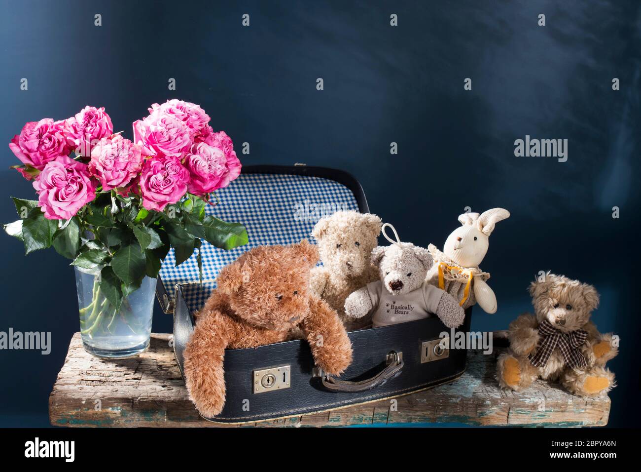 Un bouquet di rose rosse in vaso di vetro e vecchio porta una valigia vintage su uno sfondo blu e due pere e su una superficie in legno rovinato della panca Foto Stock
