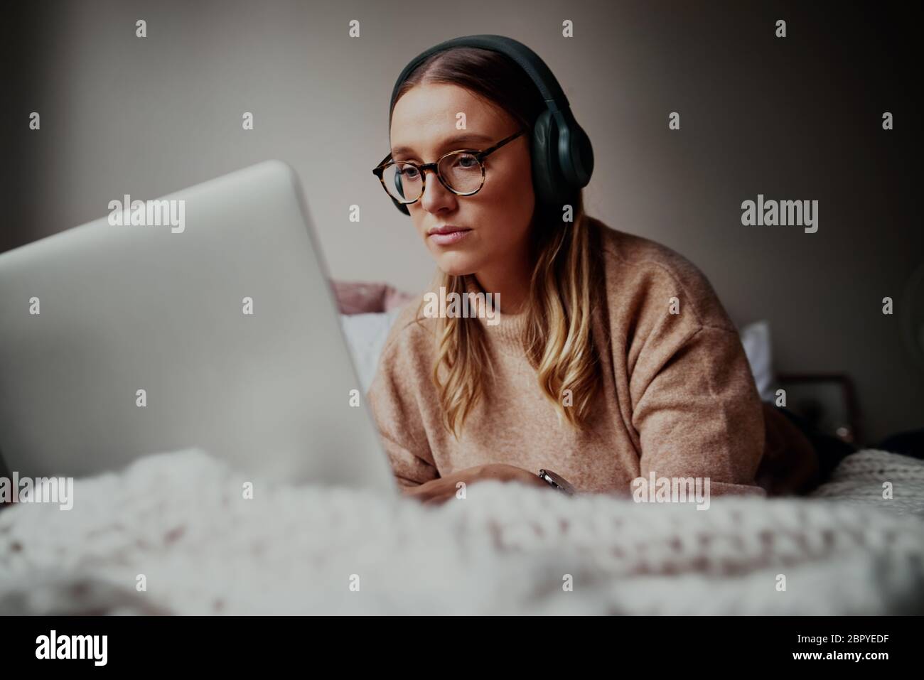 Giovane donna con occhiali che indossa le cuffie durante una videochiamata online a casa durante l'isolamento - giovane studentessa che frequenta lezioni online Foto Stock