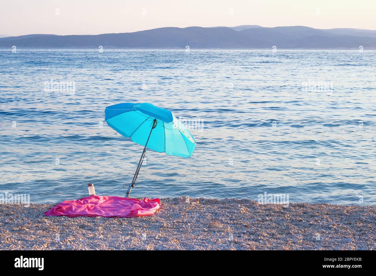 Ombrellone blu sulla costa estiva. Spiaggia di mare con ombrellone aspetta i turisti al tramonto. Concetto di vacanza estiva felice. Foto Stock