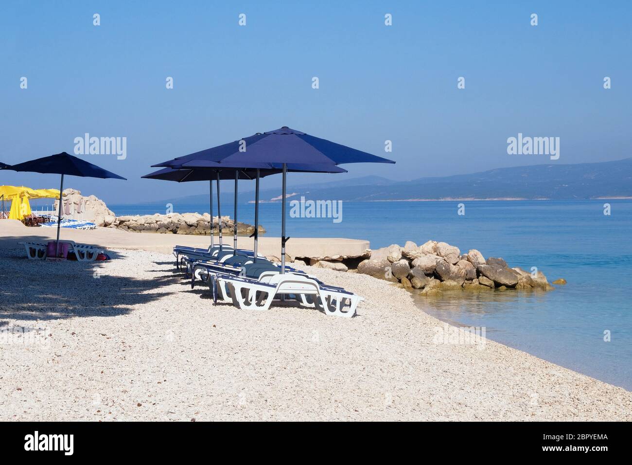 Ombrelloni e sdraio blu per rilassarsi e comfort in località balneare. Vacanze estive e viaggi per il mare. Servizio a pagamento sulle spiagge di comfort. Foto Stock