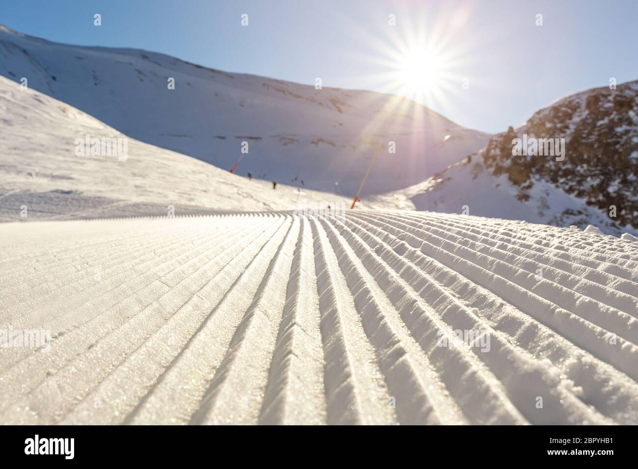 Ranghi retti retti di piste da sci preparate di recente con sole luminoso e cielo blu chiaro sullo sfondo. Montagna innevata Foto Stock