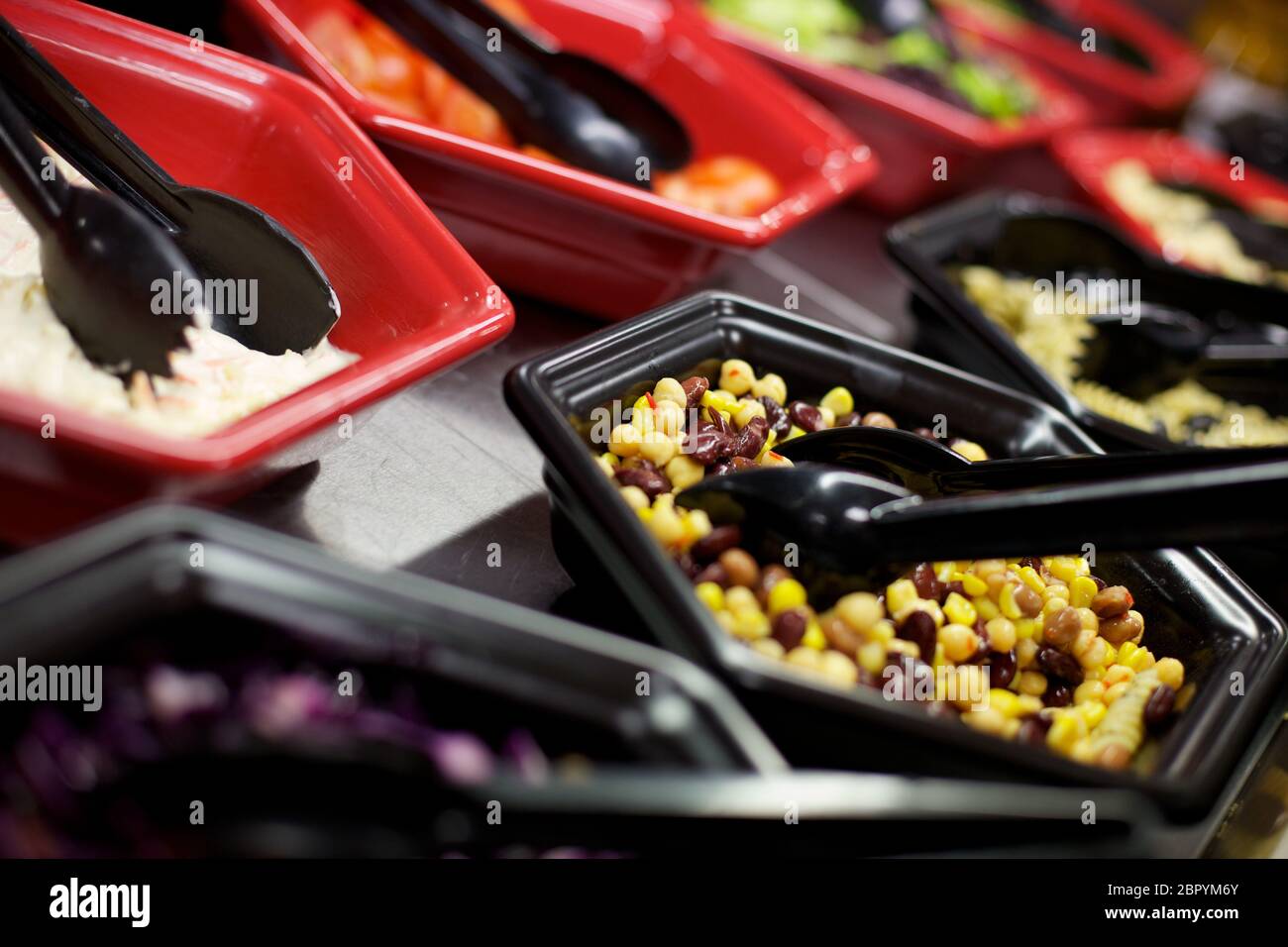 Ciotole nere e rosse con tenaglie nere ripieni di diversi ingredienti per insalata, Foto Stock