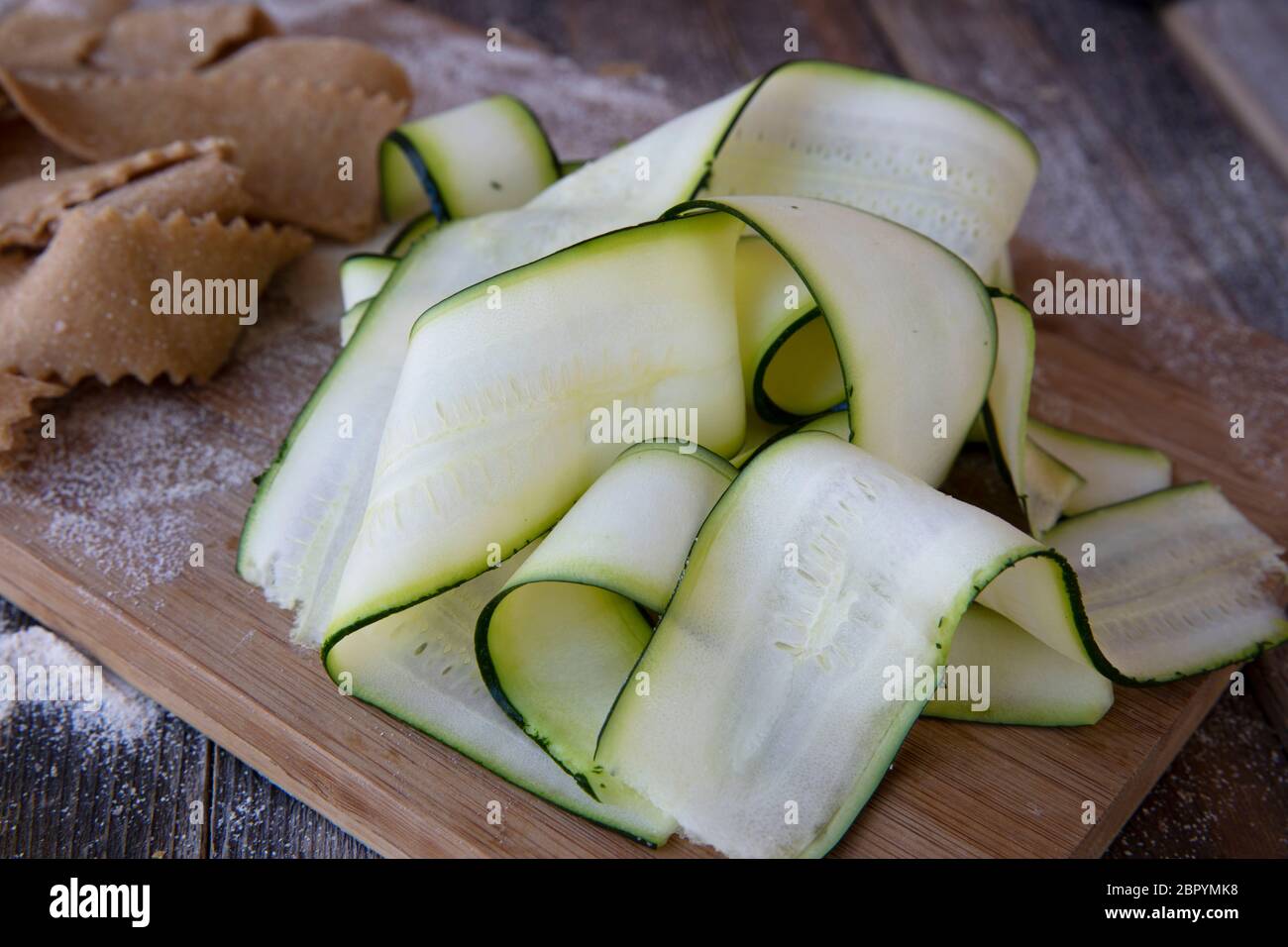 Fresco tagliato nastri di zucchine sul tagliere con pappardell fatti in casa la pasta in background. Foto Stock