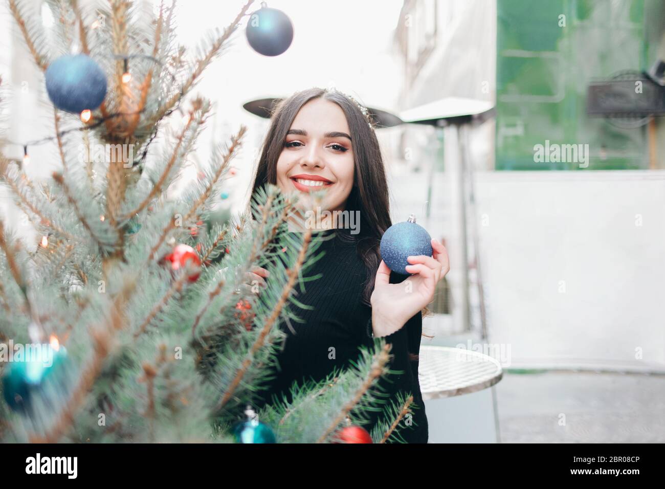 Sorridente ragazza con una palla di albero di Natale per ha un buon umore di natale. Ritratto di una bella ragazza con un giocattolo di Natale in mano vicino ad un abete Foto Stock