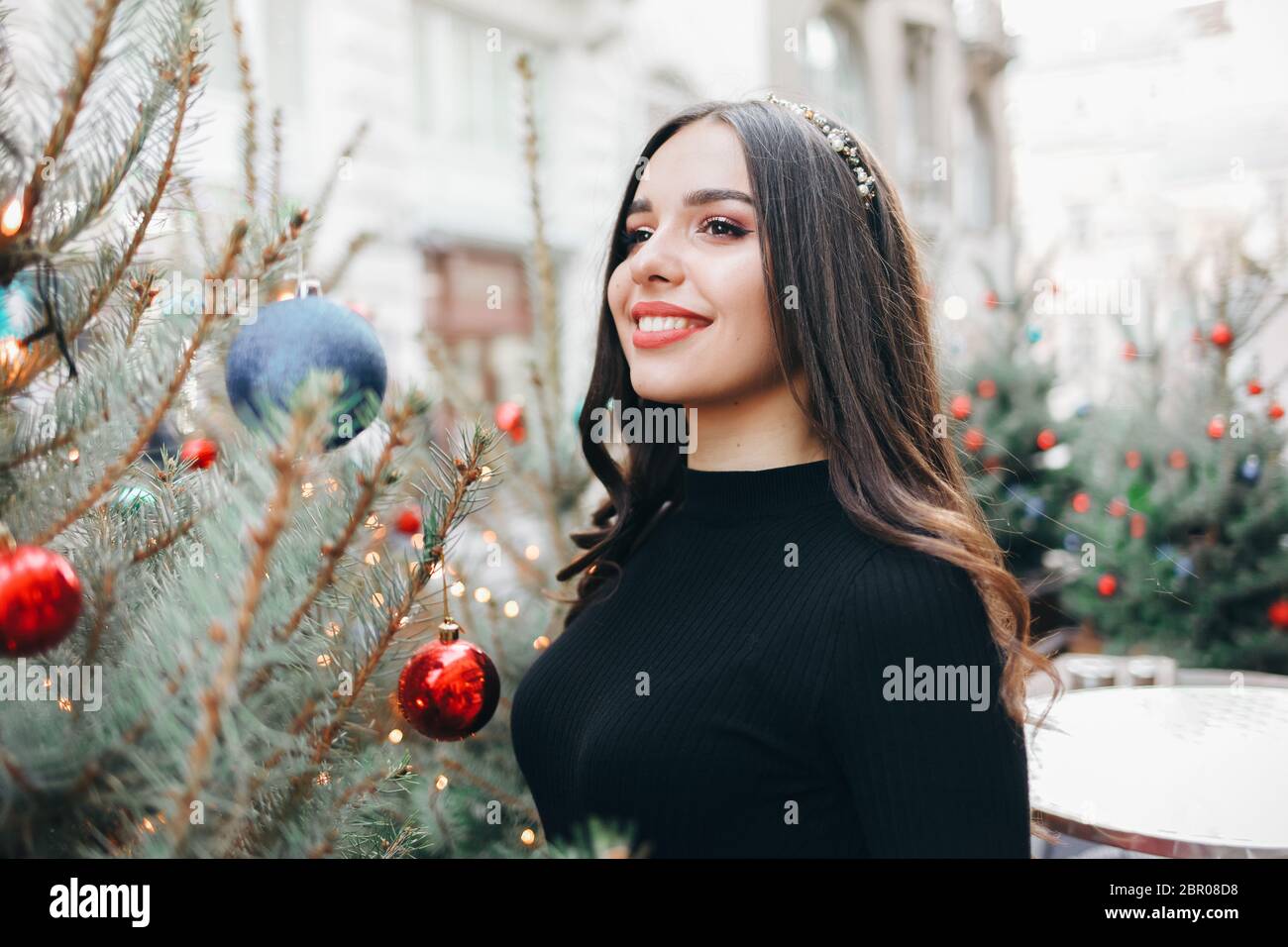 Sorridente ragazza con una palla di albero di Natale per ha un buon umore di natale. Ritratto di una bella ragazza con un giocattolo di Natale in mano vicino ad un abete Foto Stock