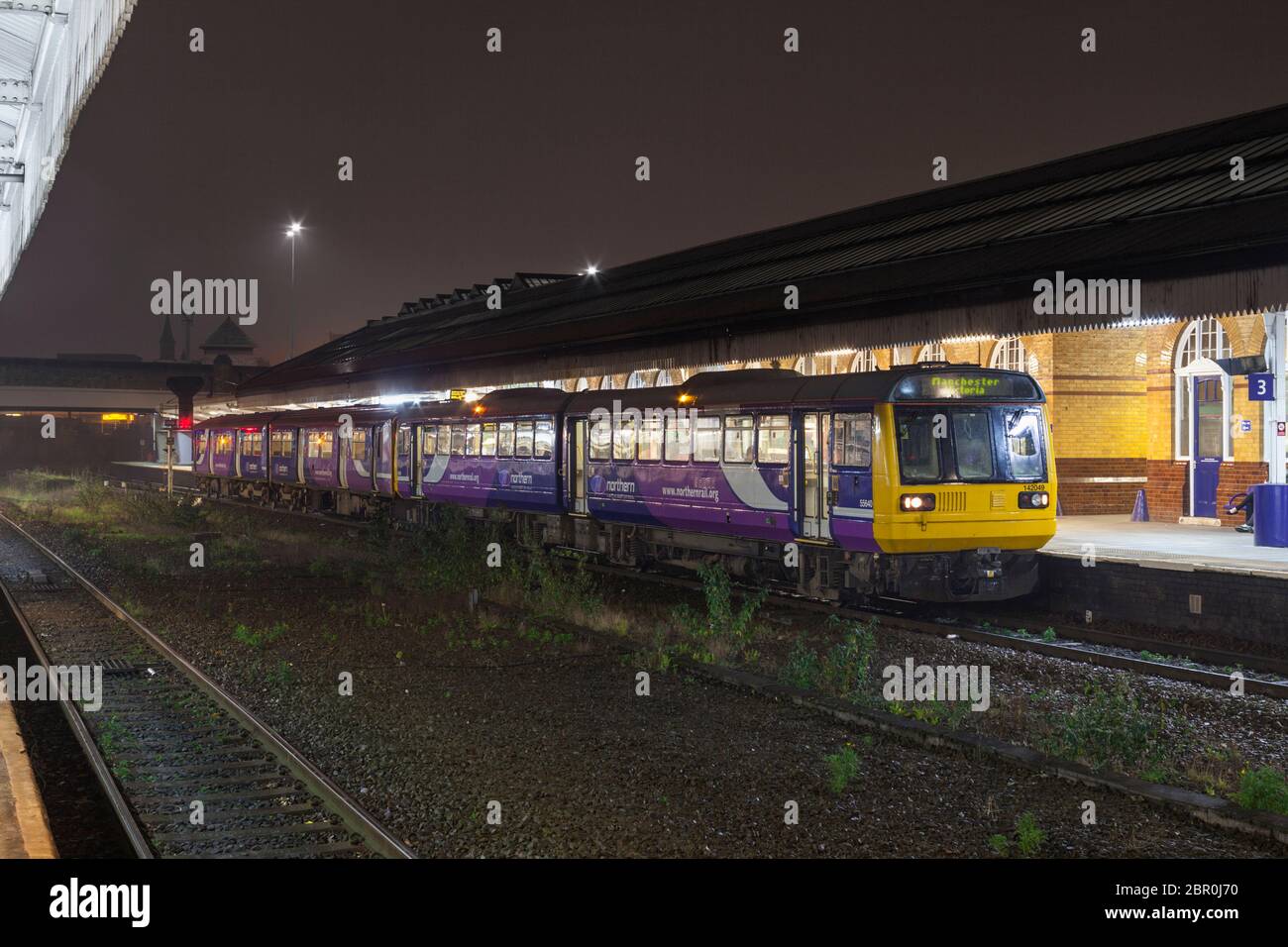 Il treno 142 della Northern Rail classe 142049 conduce lo sprinter classe 150 150206 alla stazione di Bolton in una notte buia sotto la pioggia Foto Stock
