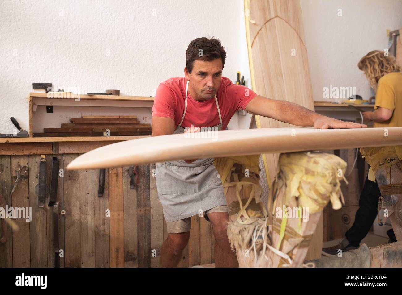 Due produttori caucasici di tavole da surf maschili che fanno insieme una tavola da surf in legno e la ispezionano Foto Stock