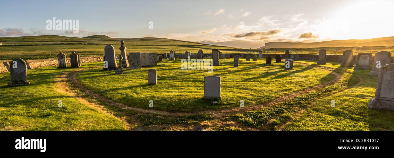 Panorama di vecchio cimitero collinoso pieno di lapidi sulla Shetland (Scozia, Regno Unito) su un magico tramonto con una luce calda drammatica e un prato verde Foto Stock