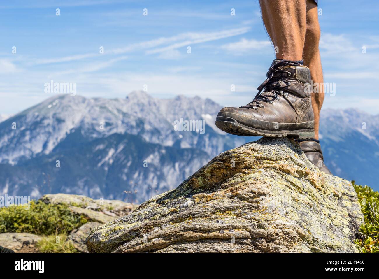 Scarpa da trekking in pelle di un uomo che si stette su una piccola roccia nella Valle Ziller, Austria. Raggiungere la vetta con una bella catena montuosa alpina nella b Foto Stock