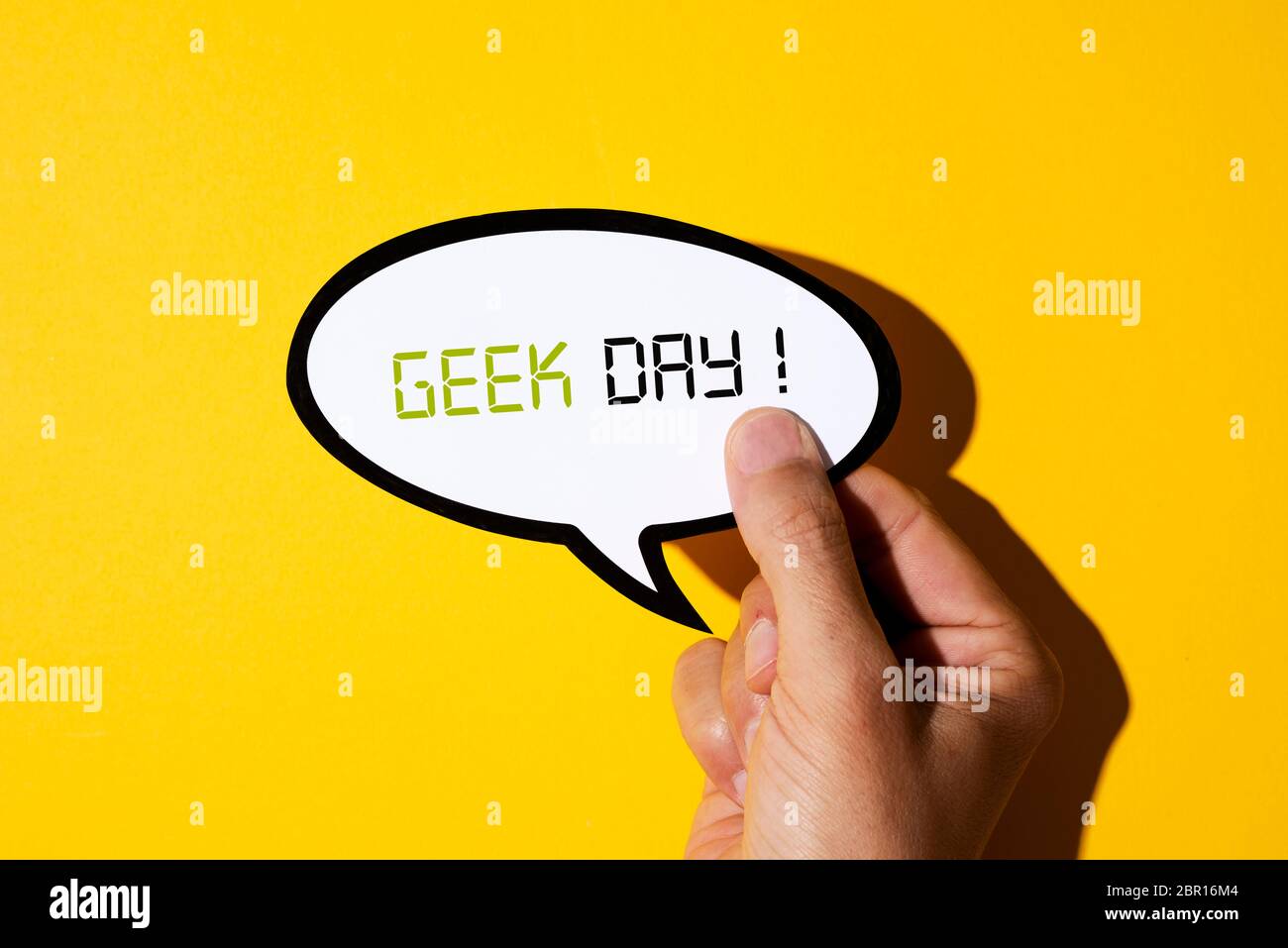 primo piano della mano di un giovane caucasico che mostra un pallone di discorso, con il testo giorno geek scritto in esso, su uno sfondo giallo Foto Stock