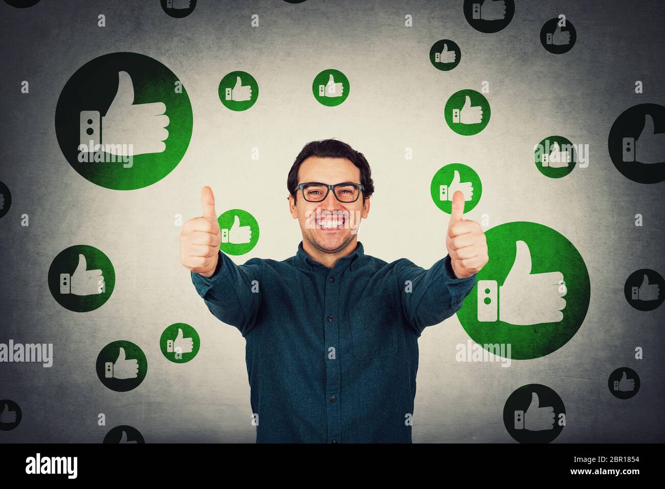 Un uomo d'affari allegro mostra i pollici verso l'alto gesto positivo, guarda la telecamera isolata sopra la parete grigia. Persona di affari che indossa gli occhiali, sorridendo ampiamente, un Foto Stock