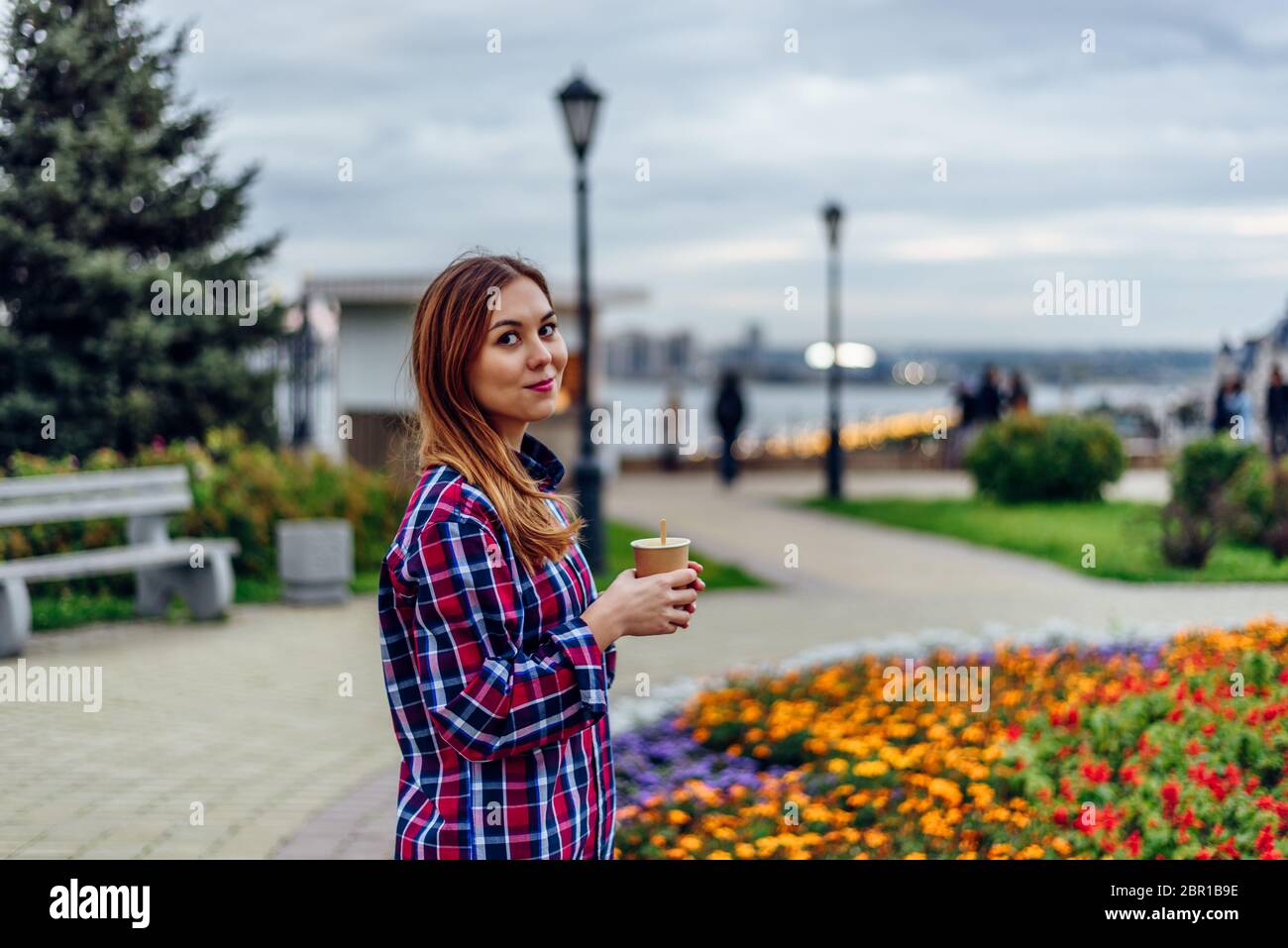 Caffè sul andare. Bella giovane donna azienda tazza da caffè e sorridente nel parco Foto Stock