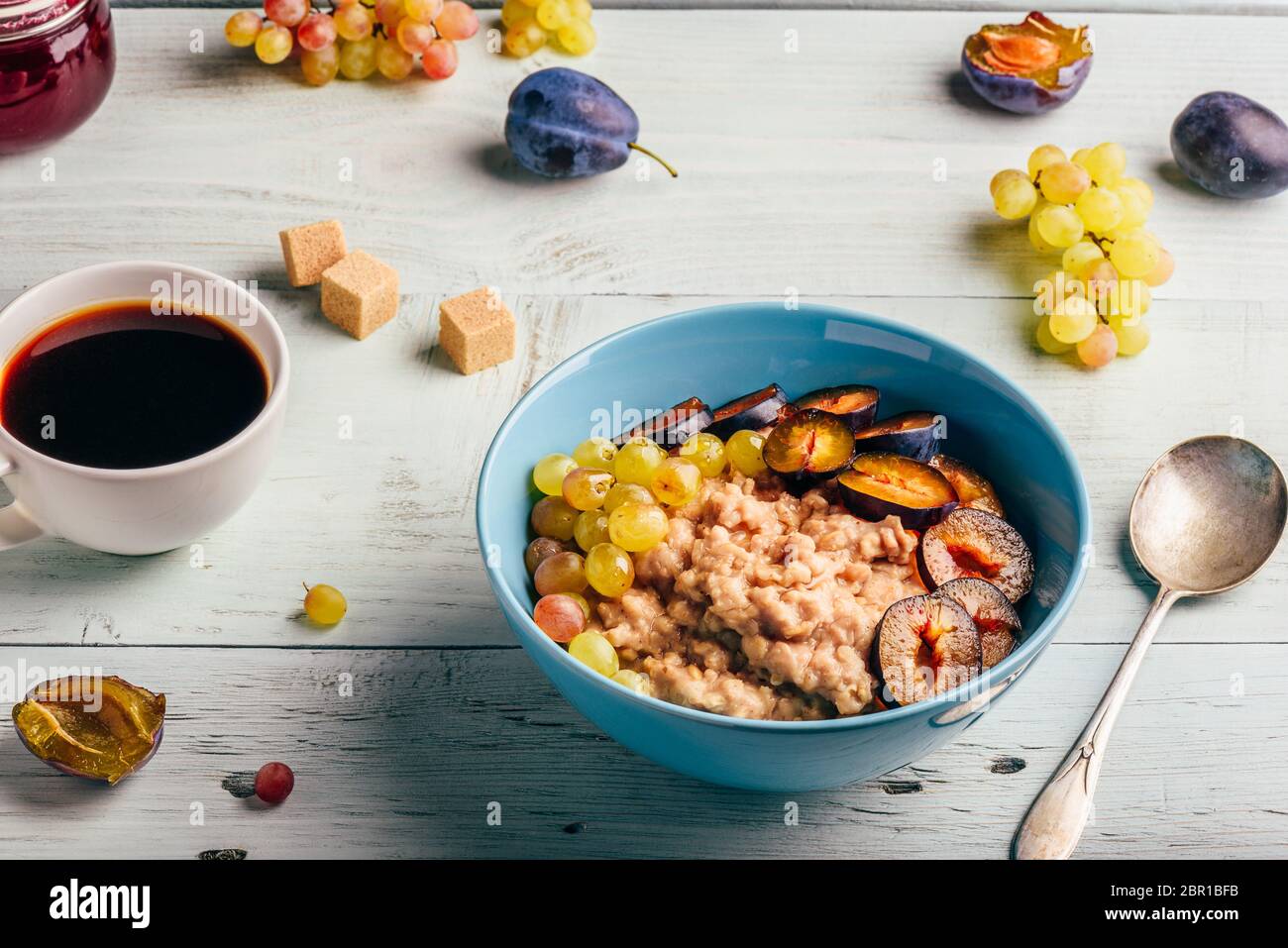 Colazione sana nozione. Porridge con prugna fresca, verde UVA e la tazza di caffè. Gli ingredienti sopra lo sfondo di legno. Foto Stock