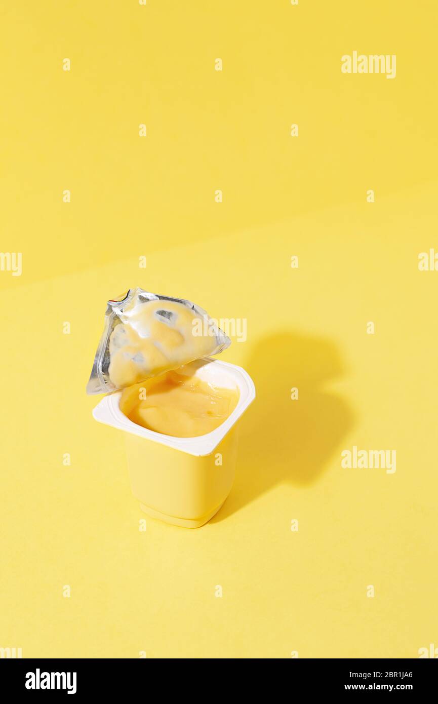 Banana e vaniglia budino o yogurt tazza di plastica su sfondo giallo pastello.concetto astratto minimo di cibo Foto Stock