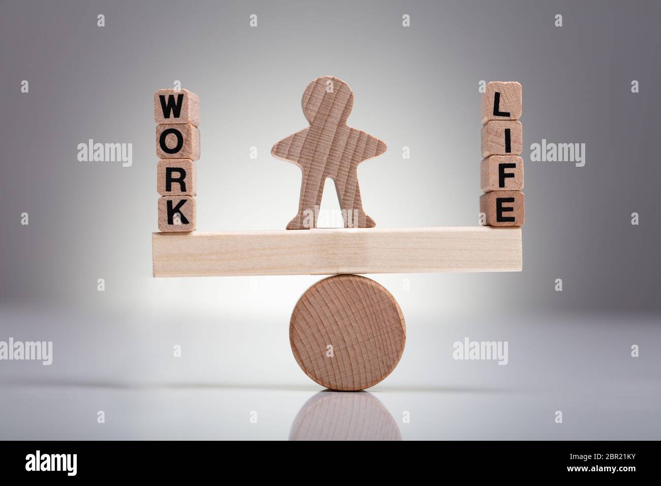 Figura umana di trovare un equilibrio tra il lavoro e la vita su altalena in legno contro uno sfondo grigio Foto Stock