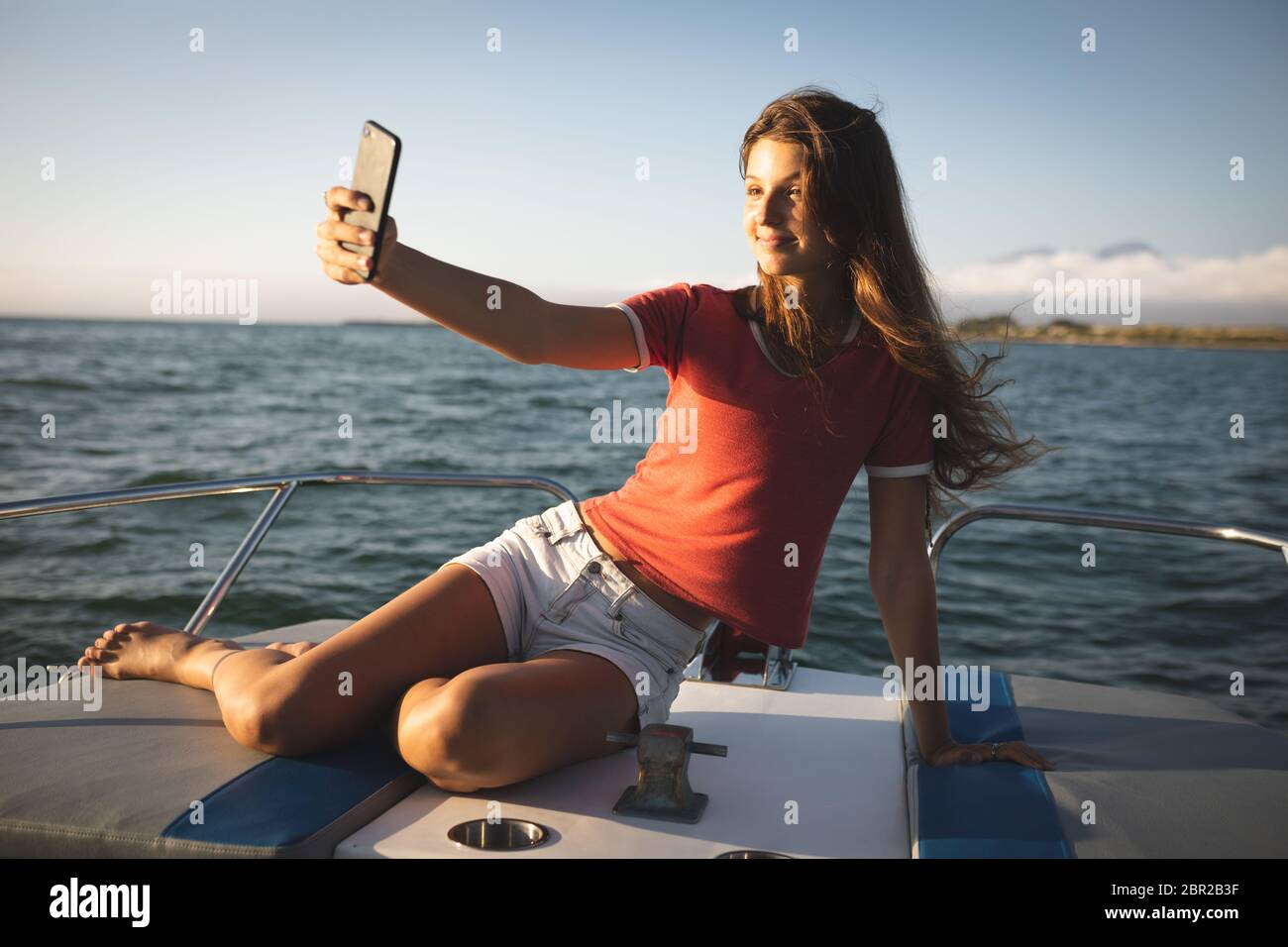 Una ragazza caucasica adolescente seduta su una barca e prendendo un selfie Foto Stock