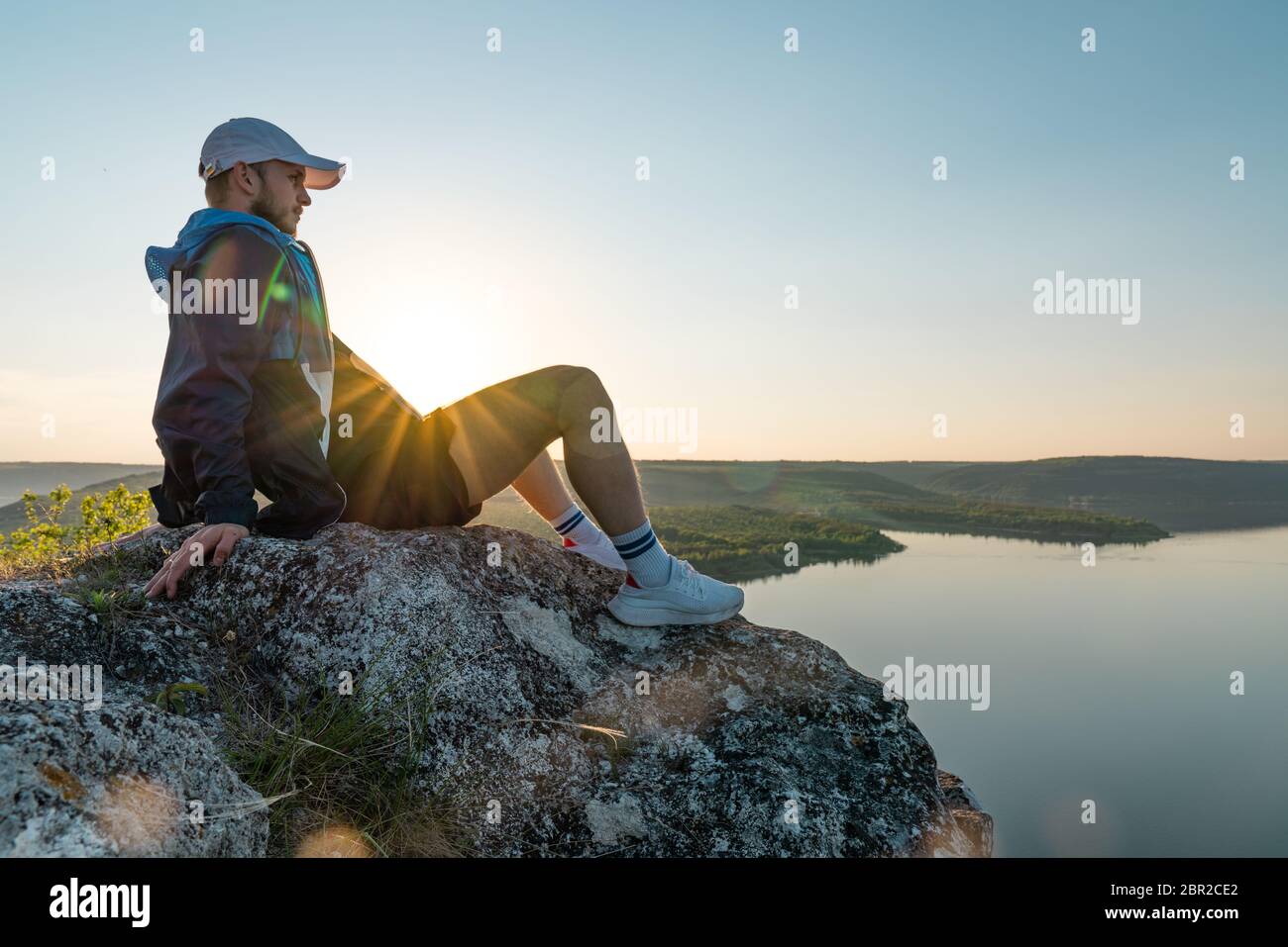 Uomo in abbigliamento sportivo e cappello su una cima di roccia ower splendido paesaggio del fiume canyon Foto Stock