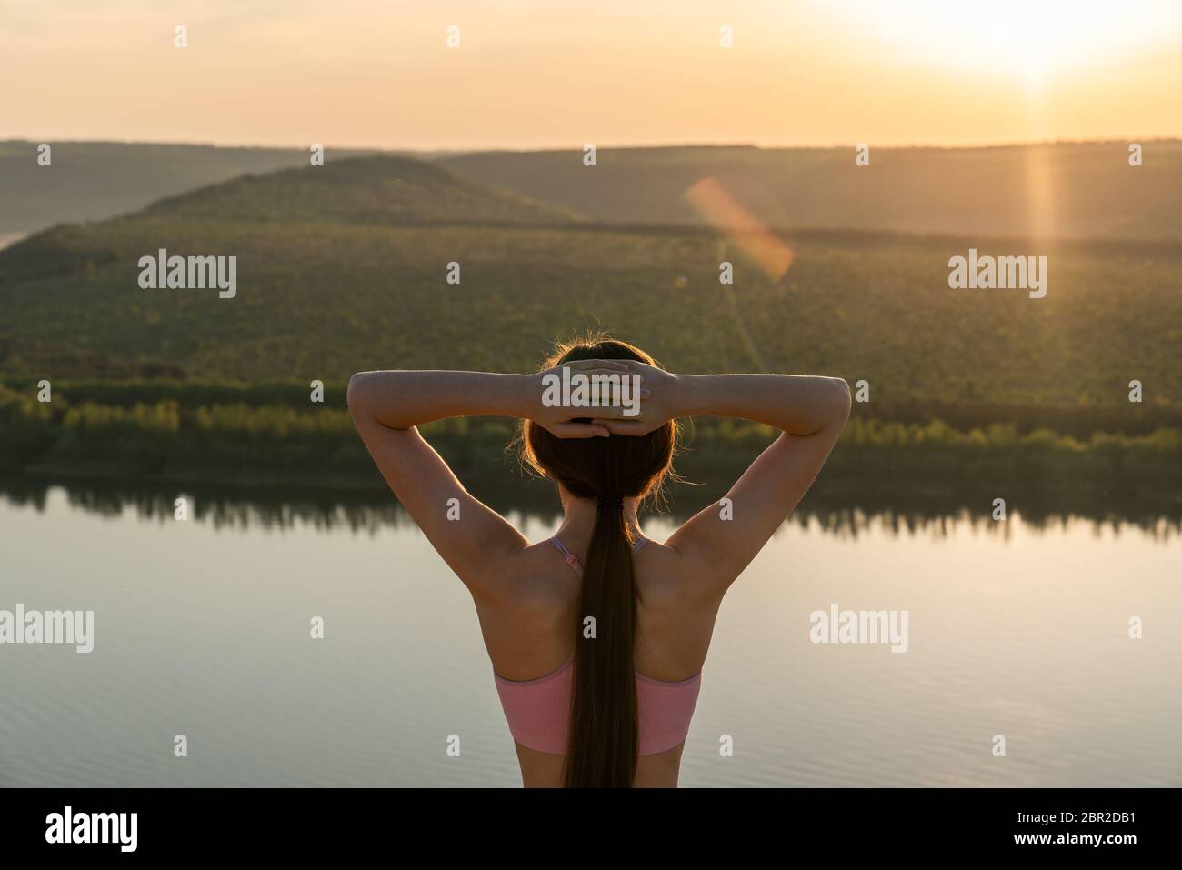 In vita ritratto di una bella donna bruna sportiva che si alza alla fotocamera tiene le mani sulla testa e godendo behinde tramonto Foto Stock
