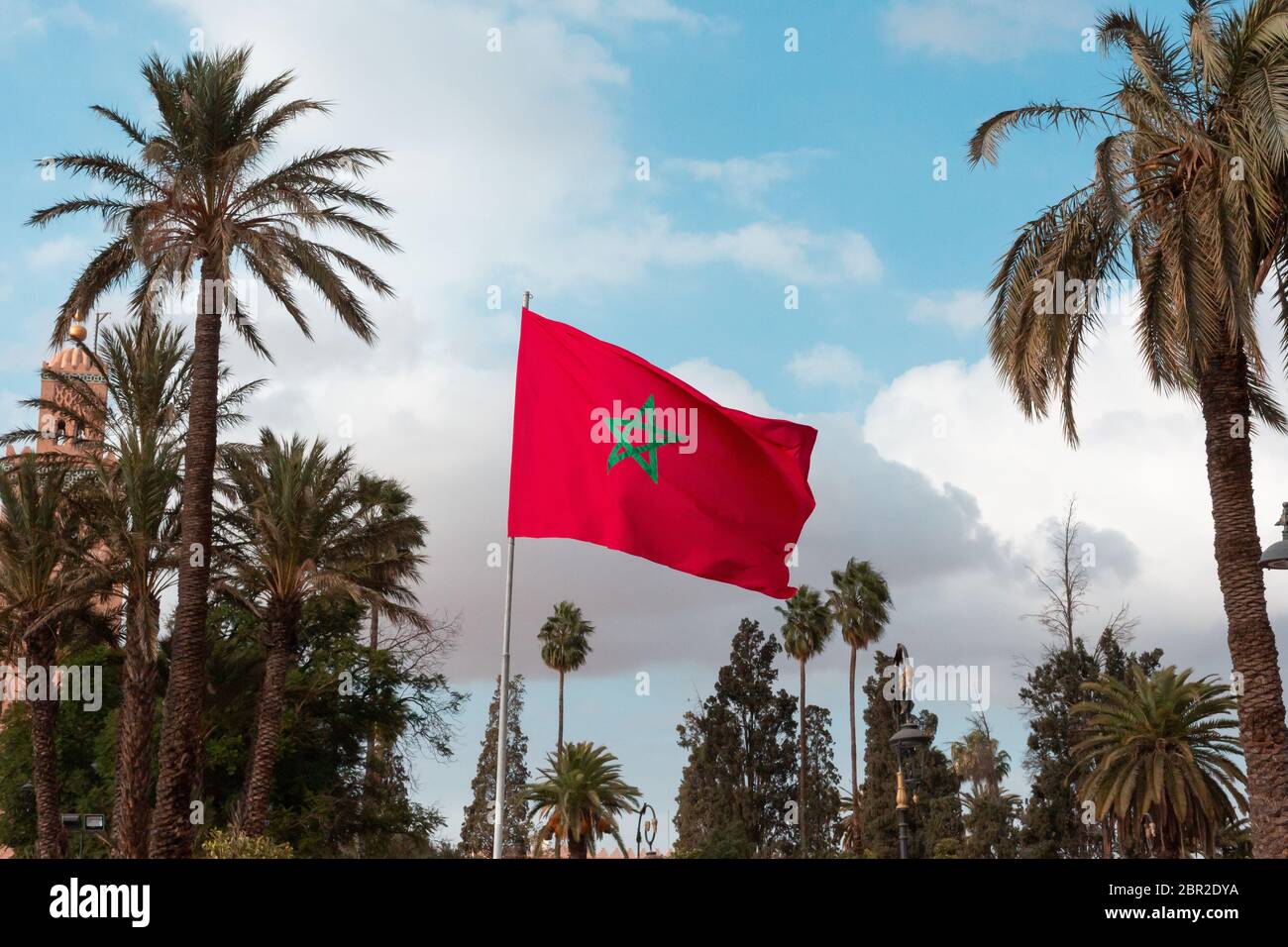 Bandiera del Marocco che svanita, con cielo blu e nuvole sullo sfondo e palme sui lati Foto Stock