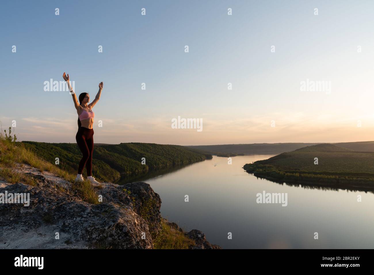 Giovane escursionista in abbigliamento sportivo si alza con le mani sollevate sulla roccia sulla collina Foto Stock