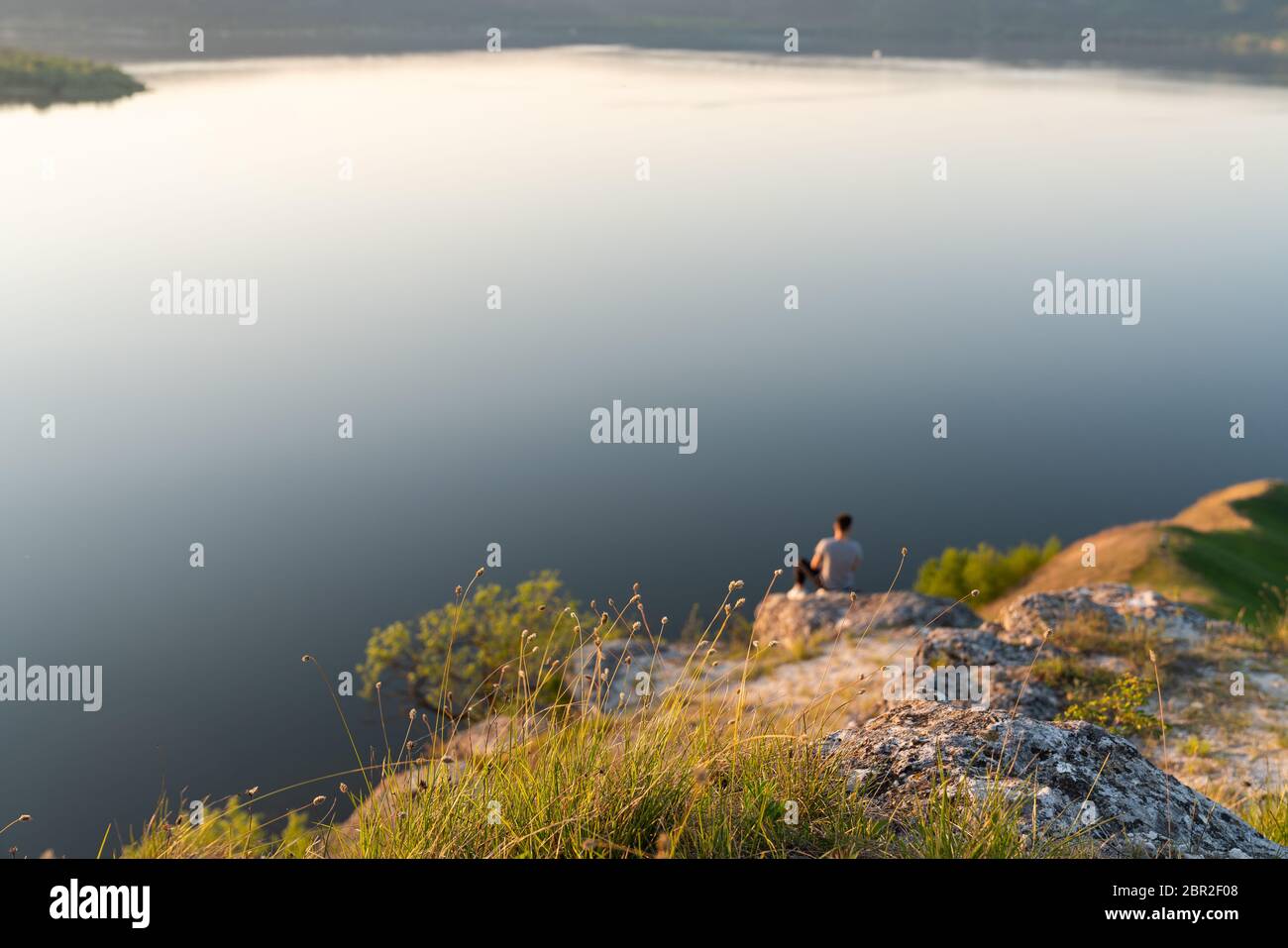 Foto sfocata, giovane maschio seduto sulla roccia e godendo di un bellissimo paesaggio di montagne fiume Foto Stock