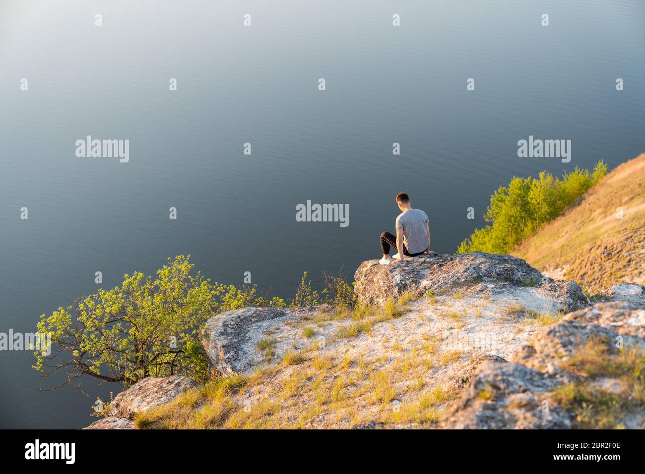 Giovane uomo in abiti casual seduto alla telecamera sulla roccia Foto Stock