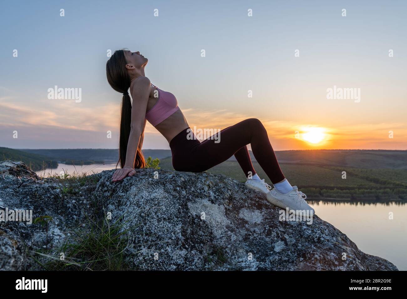 Giovane donna sana in elegante abbigliamento sportivo pratica yoga sulla cima della montagna scogliera Foto Stock