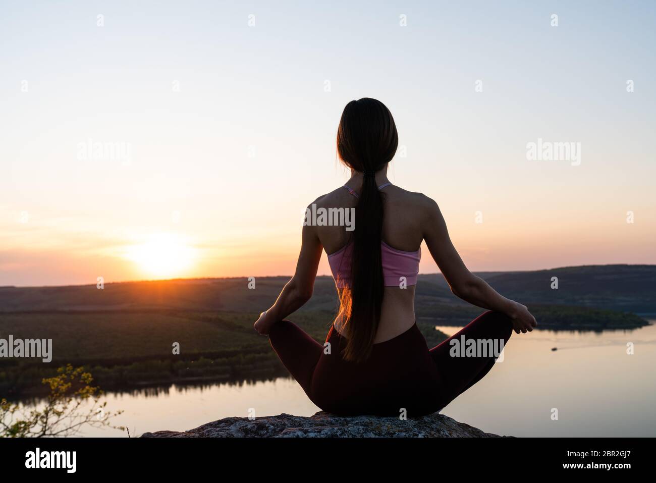 Vista della giovane donna che esercita yoga all'alba sul lago, meditazione persone concetto di serenità e benessere nella vita, lotus yoga posizione Foto Stock