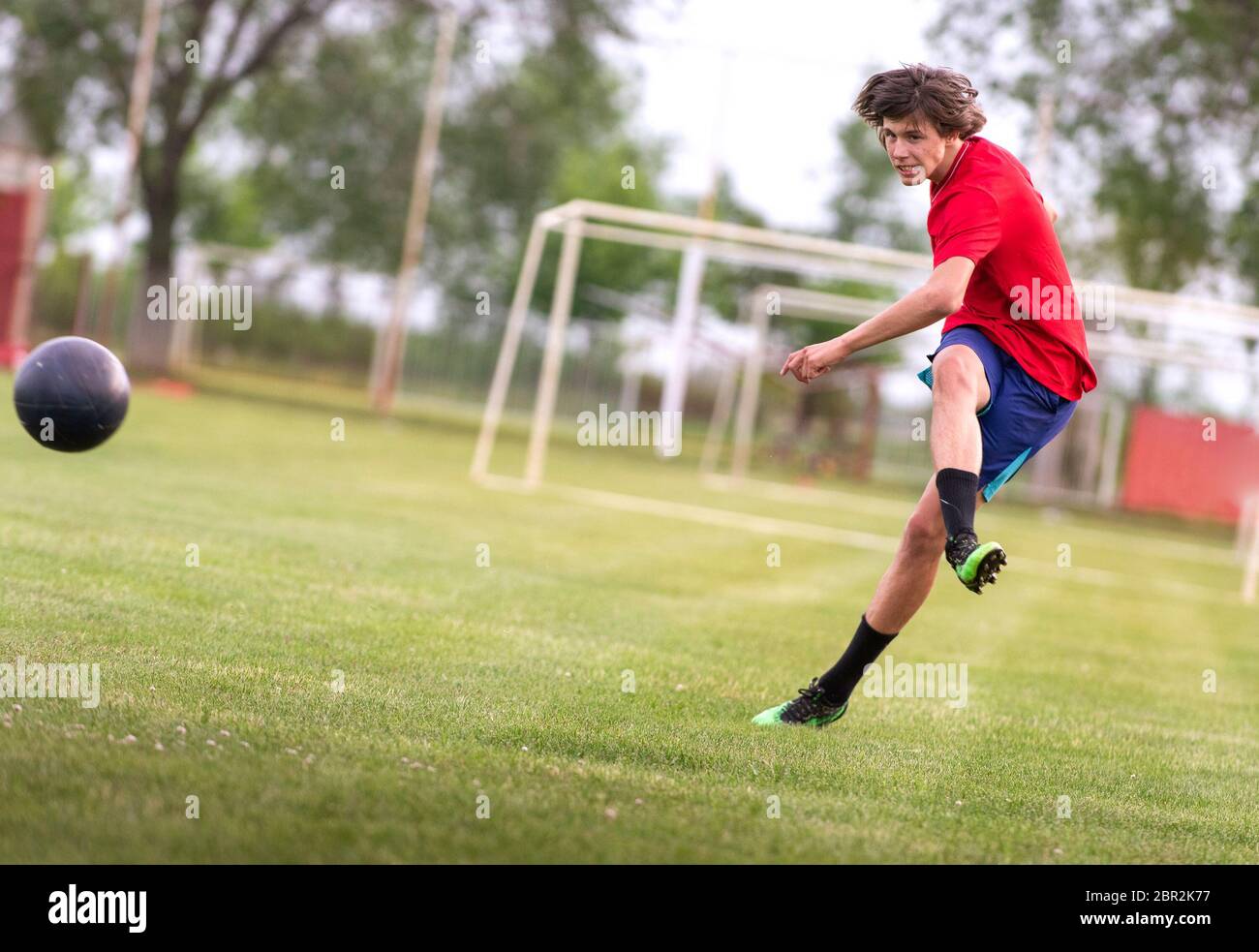 Il giocatore di calcio adolescente calcia la palla in un obiettivo Foto Stock