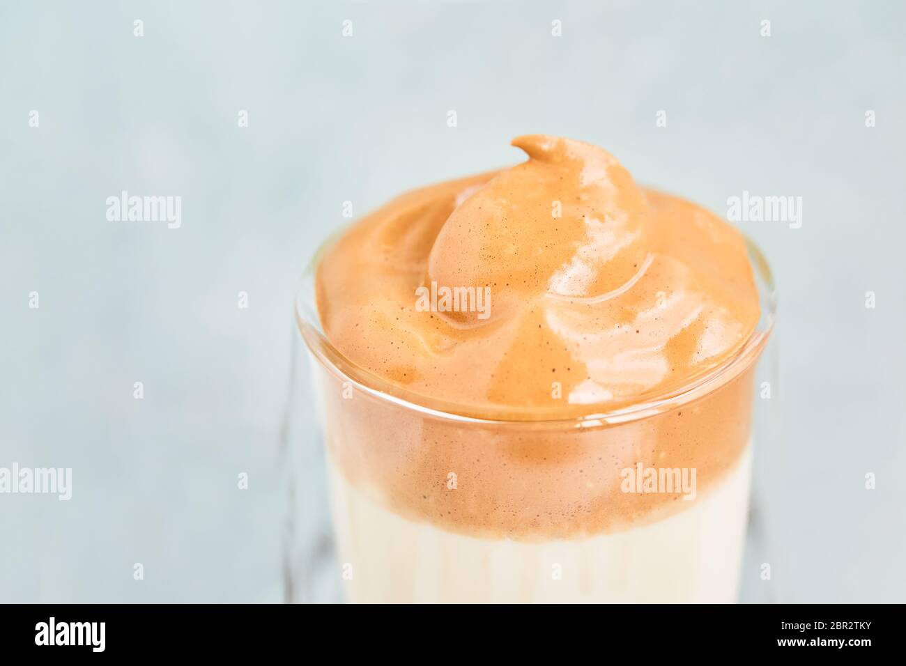 Il caffè Dalgona viene preparato in un bicchiere trasparente su sfondo azzurro. Spazio di copia per testo, messa a fuoco selettiva Foto Stock